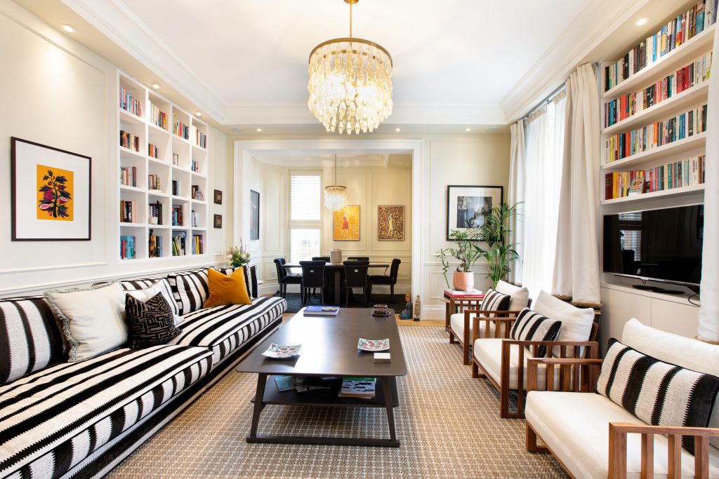 Spacious modern living room with black and white upholstered sofas and armchairs, dining table, and original artwork on the walls