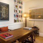 Elegant home study featuring bespoke floor-to-ceiling bookcases, a leather-inset writing desk, sculptural floor lamp, and original artwork on the walls